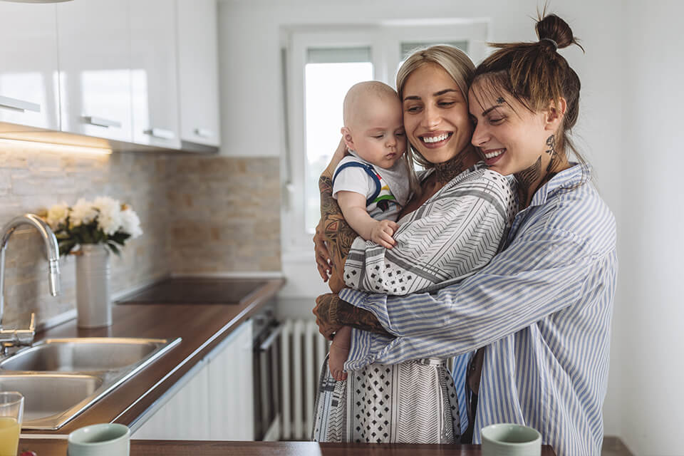 Two ladies hugging a baby in a kitchen