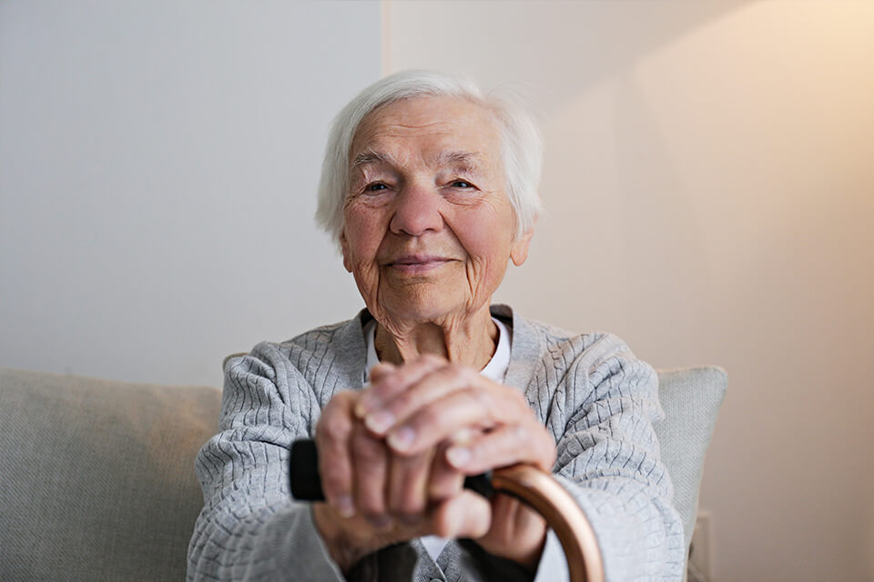 A old lady with a walking stick smiling at the camera