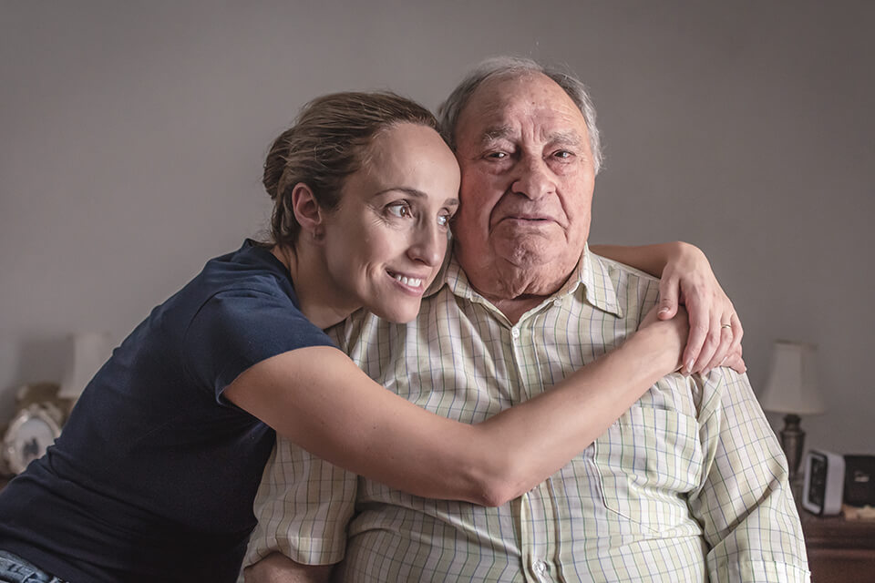 A younger woman hugging an older man and they are both smiling.